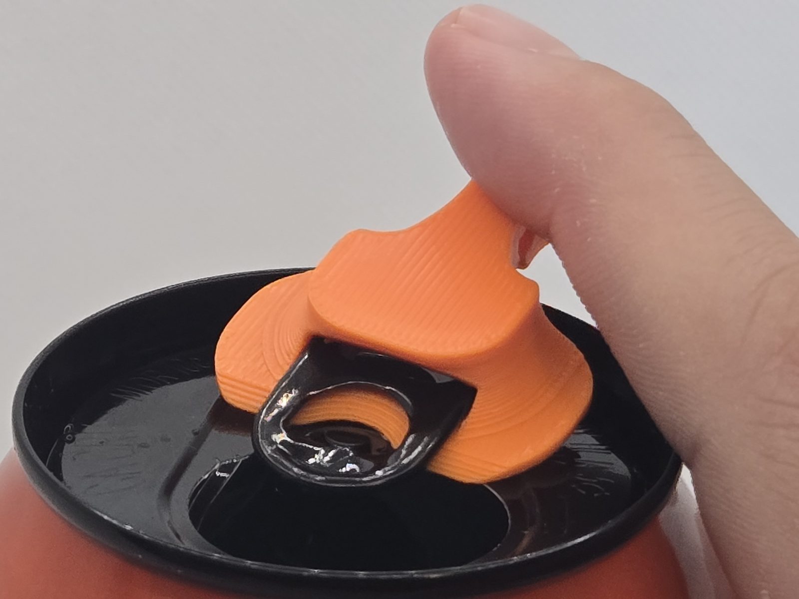 Macro of the can cover's slot sitting over the pull tab - the capture that keeps it attached to the can and lets it turn