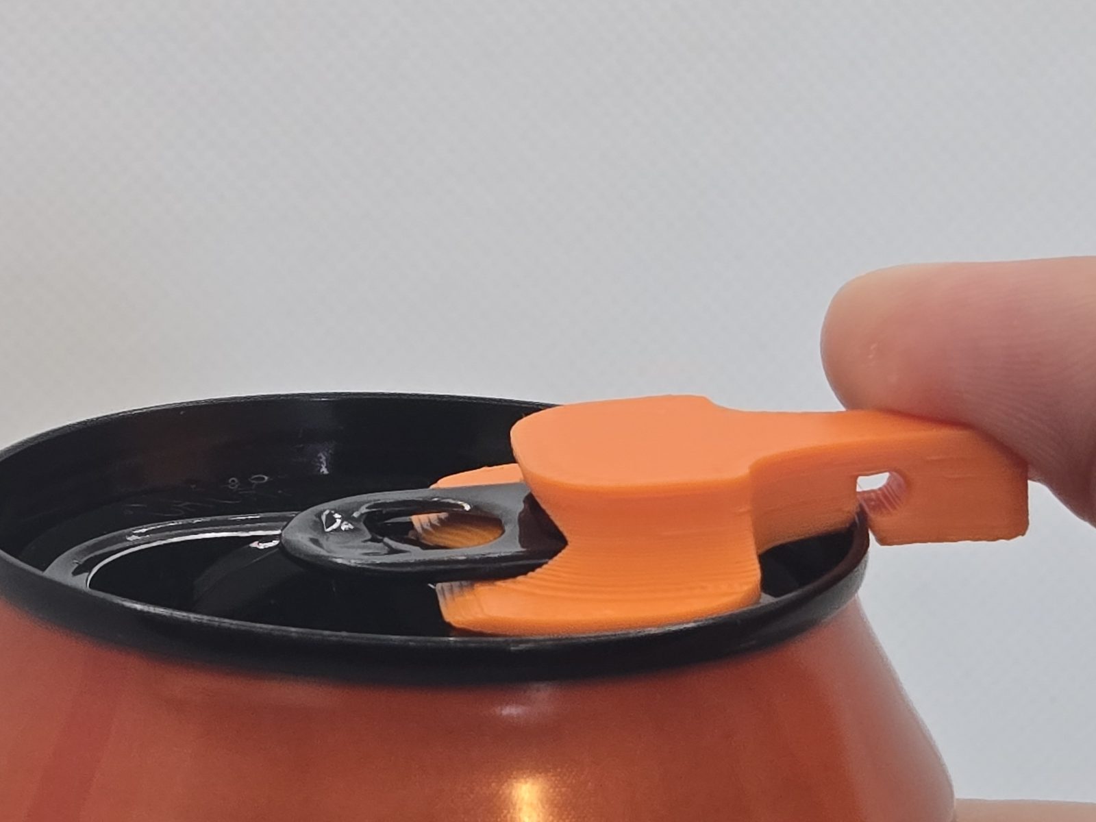 Spinning the cover around the pull-tab so its body sits over the can opening, keeping bugs and debris out of the drink
